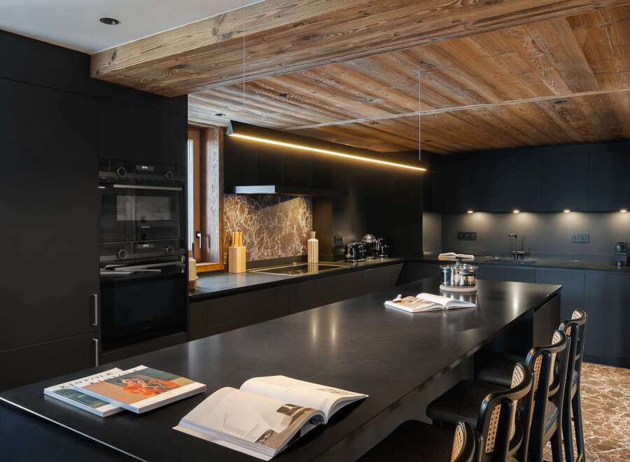This modern kitchen boasts sleek black cabinetry and a stunning wooden ceiling, creating a sophisticated and inviting atmosphere.
