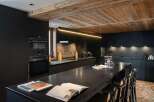 This modern kitchen boasts sleek black cabinetry and a stunning wooden ceiling, creating a sophisticated and inviting atmosphere.