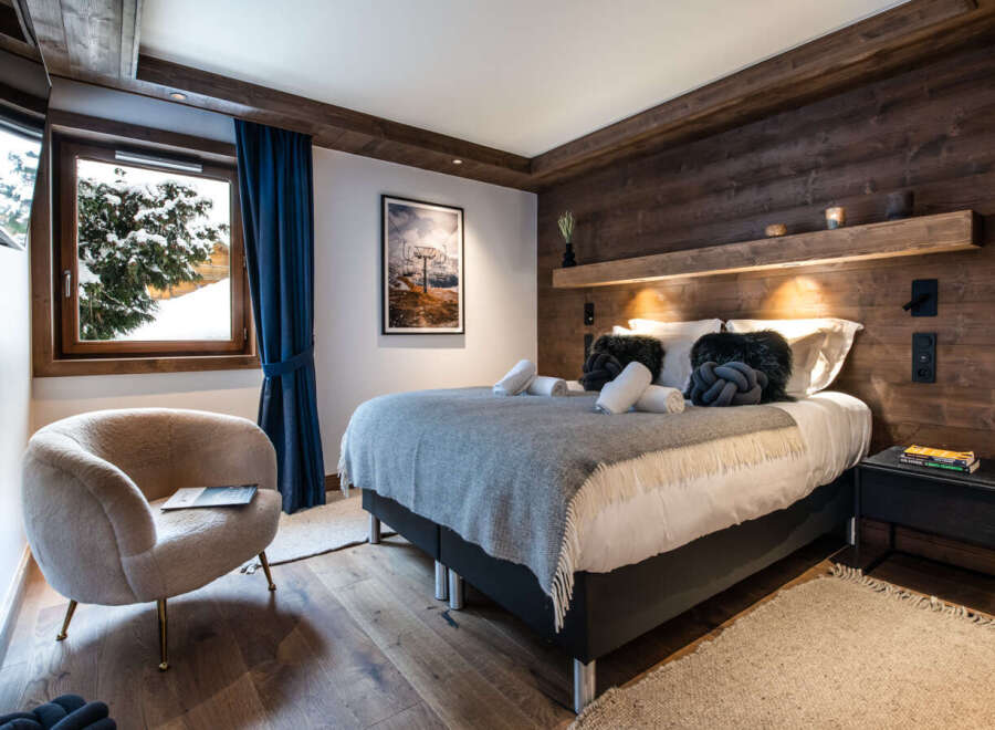 This luxurious bedroom boasts a cozy atmosphere with a plush sheepskin armchair and a comfortable bed dressed in soft grey linens.
