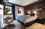 This luxurious bedroom boasts a cozy atmosphere with a plush sheepskin armchair and a comfortable bed dressed in soft grey linens.