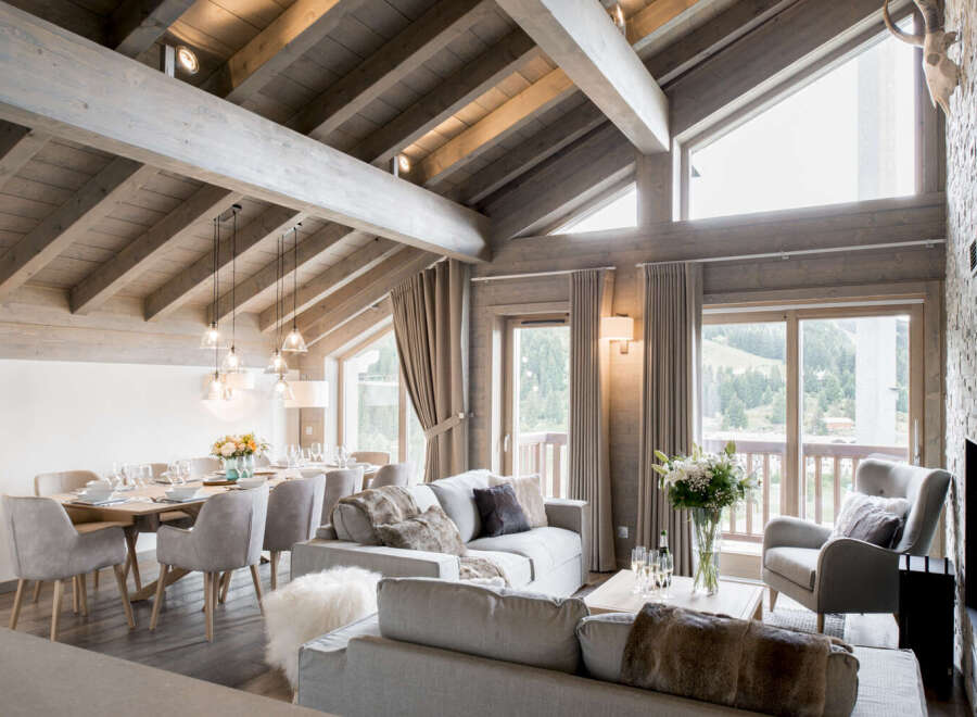 This stunning chalet boasts a spacious open-plan living area with exposed wooden beams, large windows offering breathtaking mountain views, and a cozy fireplace.