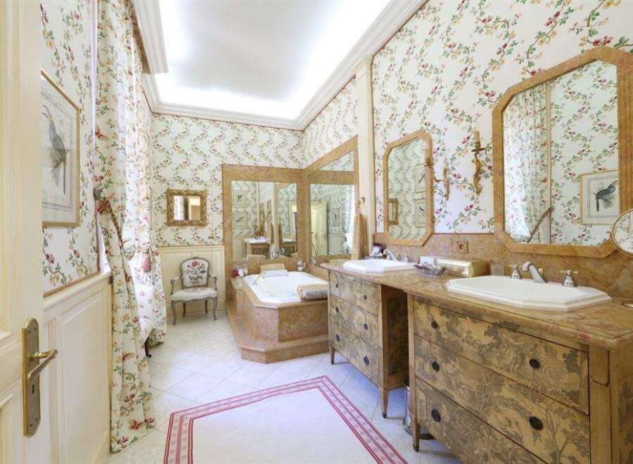 This luxurious bathroom boasts elegant floral wallpaper, antique-style vanities, and a spacious bathtub.