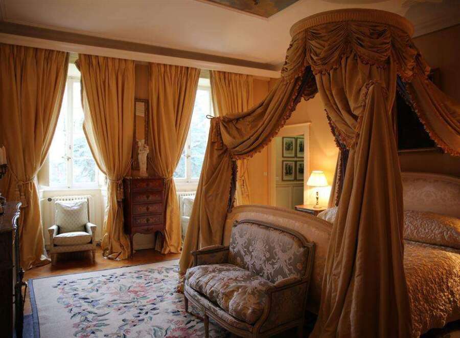 Luxurious bedroom with a four-poster bed draped in rich fabrics, complemented by elegant gold curtains and a plush seating area.
