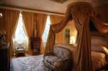 Luxurious bedroom with a four-poster bed draped in rich fabrics, complemented by elegant gold curtains and a plush seating area.