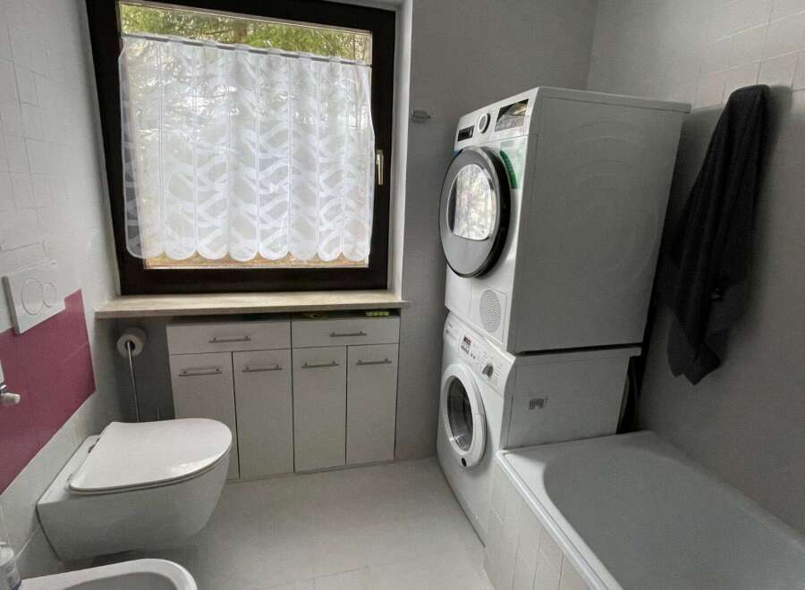 This bathroom features a modern design with a stacked washer and dryer, maximizing space.