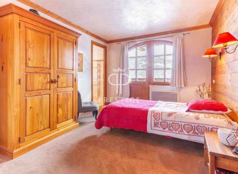 Discover the charm of this cozy bedroom, featuring a rustic wooden wardrobe and a comfortable bed with a vibrant red coverlet.