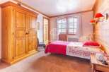 Discover the charm of this cozy bedroom, featuring a rustic wooden wardrobe and a comfortable bed with a vibrant red coverlet.