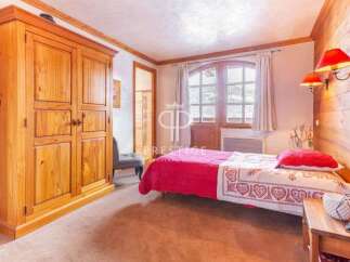 Discover the charm of this cozy bedroom, featuring a rustic wooden wardrobe and a comfortable bed with a vibrant red coverlet.