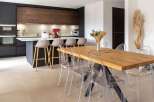 Stunning kitchen with dark cabinetry and wood accents, complemented by a spacious dining area featuring a live-edge wood table and transparent chairs.