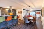 Stunning open-concept living space featuring a modern kitchen with a breakfast bar, seamlessly flowing into a dining area with a wooden table and comfortable seating.