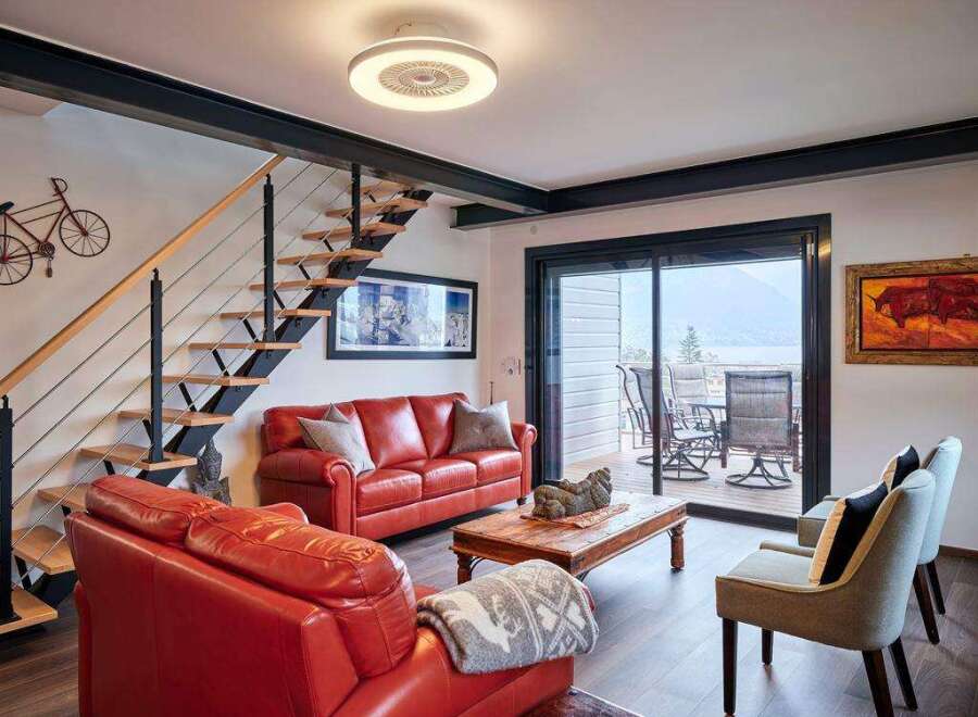 Stunning lake views from this modern living space, featuring a sleek floating staircase and comfortable red leather seating.