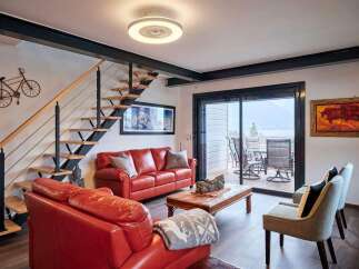 Stunning lake views from this modern living space, featuring a sleek floating staircase and comfortable red leather seating.