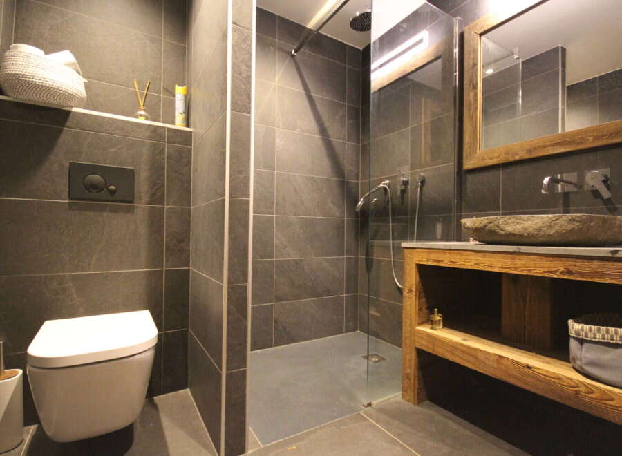 This modern bathroom features a sleek, minimalist design with dark gray tiles and a walk-in shower.