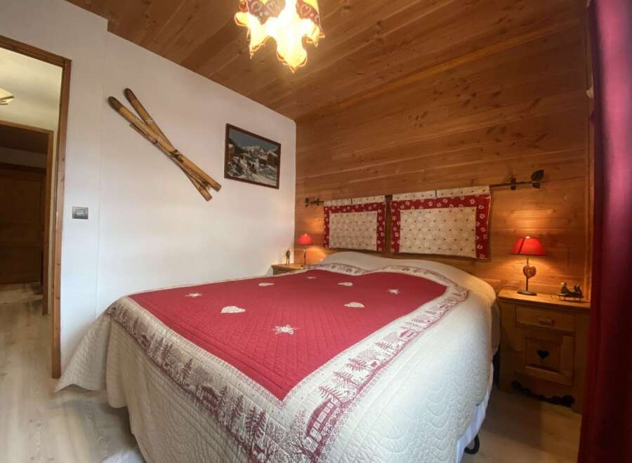 Cozy chalet bedroom with wooden walls and a comfortable double bed featuring a red and cream quilt.