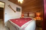 Cozy chalet bedroom with wooden walls and a comfortable double bed featuring a red and cream quilt.