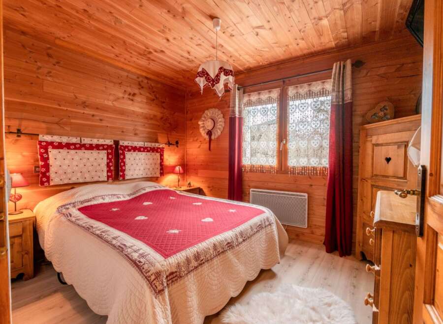 Cozy chalet bedroom with wooden walls and floors, featuring a comfortable double bed with a red and cream quilt.