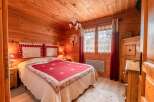 Cozy chalet bedroom with wooden walls and floors, featuring a comfortable double bed with a red and cream quilt.