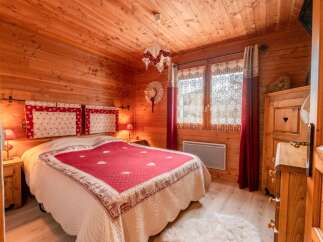 Cozy chalet bedroom with wooden walls and floors, featuring a comfortable double bed with a red and cream quilt.
