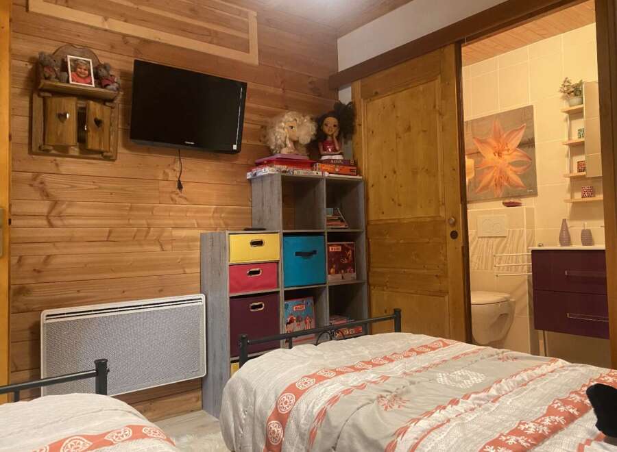 Cozy chalet bedroom with twin beds, featuring a rustic wood wall and built-in storage.