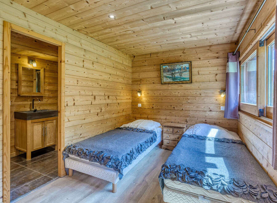 Experience rustic charm in this cozy wooden cabin bedroom, featuring two comfortable twin beds adorned with plush grey blankets.