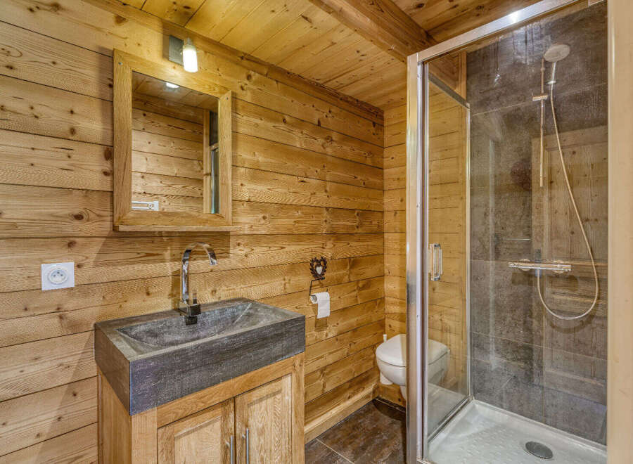 Experience rustic charm in this bathroom, featuring warm wooden walls and a modern stone sink.
