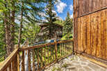Experience the charm of this rustic wooden chalet nestled amidst lush green trees and a breathtaking mountain backdrop.