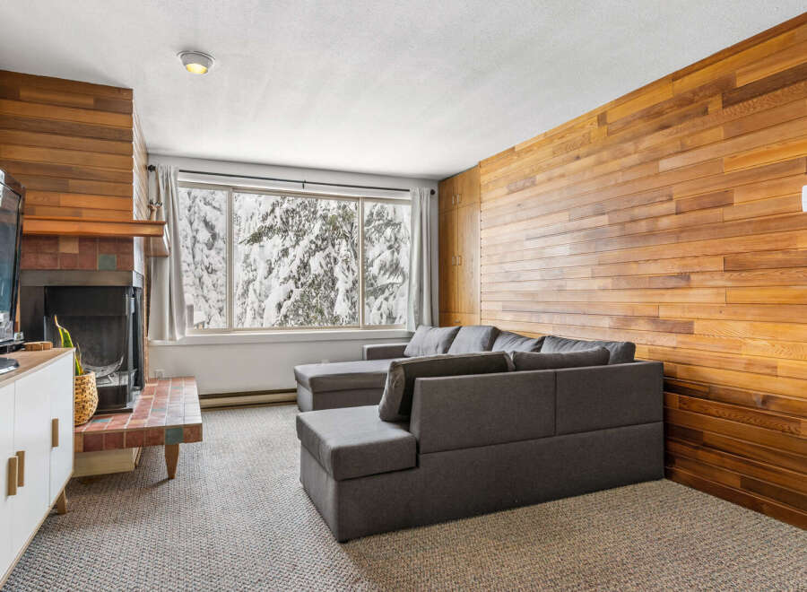 Cozy up in this charming living space! Featuring a stylish gray sectional and a warm wood-paneled wall, this room is perfect for relaxation.