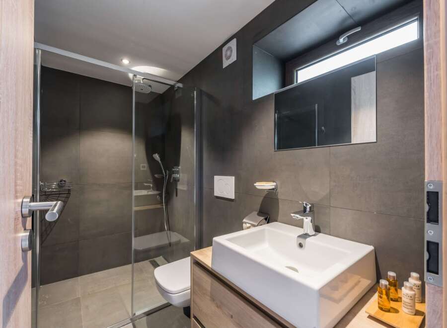 This modern bathroom features a sleek, minimalist design with dark gray tiles and a glass shower enclosure.