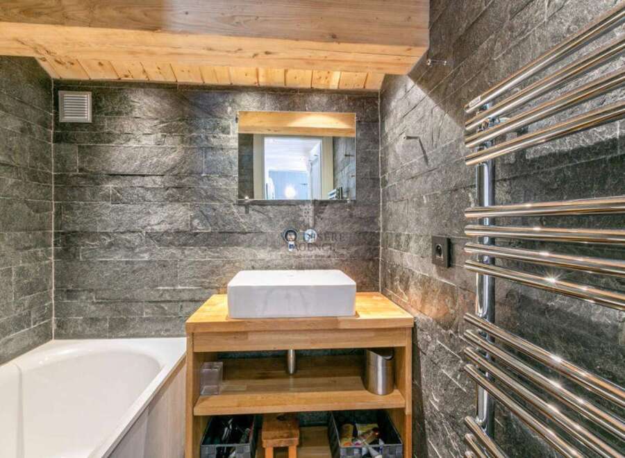 This stunning bathroom boasts a luxurious bathtub, a sleek modern sink with wooden vanity, and a heated towel rack.