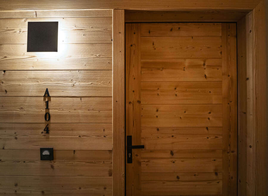 Experience rustic charm with this beautifully crafted wooden door, featuring a modern black handle and a subtle room number 'A104'.