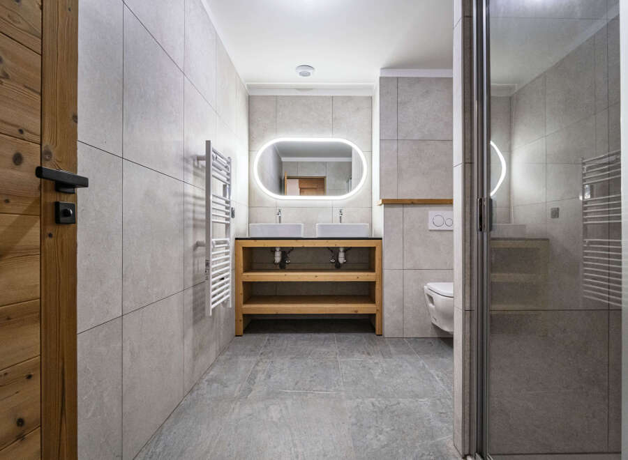 Experience modern comfort in this beautifully appointed bathroom, featuring a sleek double vanity with vessel sinks and a striking illuminated mirror.