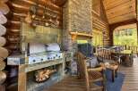 Experience luxury living in this stunning log cabin, featuring an outdoor kitchen with a built-in grill and a cozy fireplace.