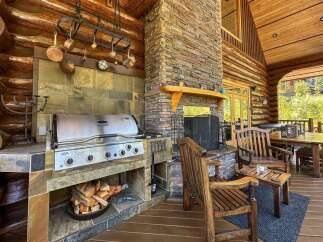 Experience luxury living in this stunning log cabin, featuring an outdoor kitchen with a built-in grill and a cozy fireplace.