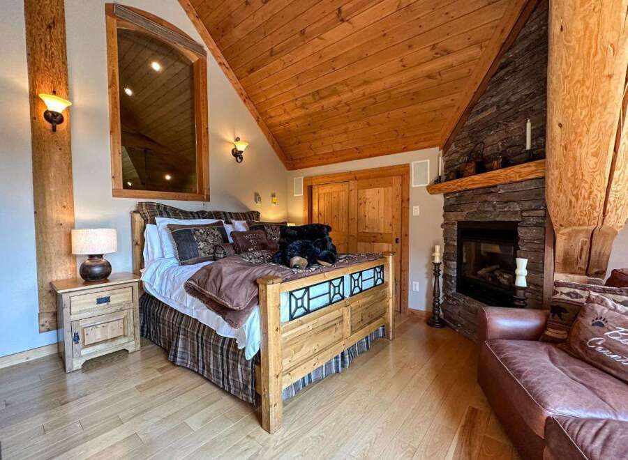 Experience rustic charm in this cozy bedroom featuring a beautiful wooden bed frame and a warm fireplace.