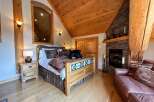 Experience rustic charm in this cozy bedroom featuring a beautiful wooden bed frame and a warm fireplace.