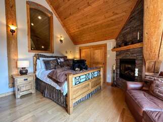 Experience rustic charm in this cozy bedroom featuring a beautiful wooden bed frame and a warm fireplace.