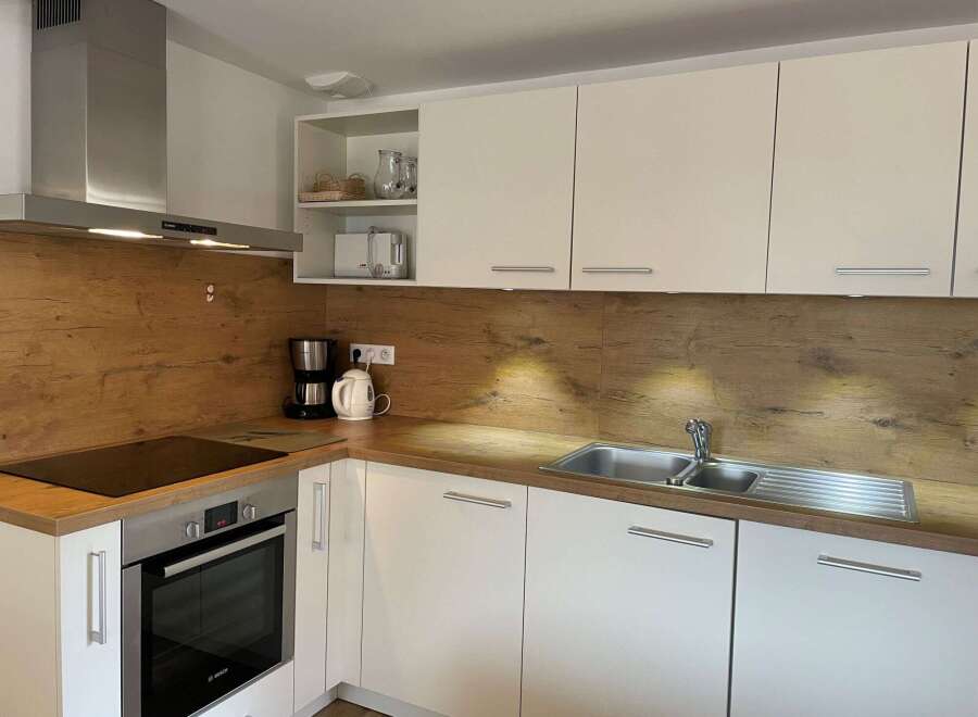 Modern kitchen with sleek white cabinets and a stylish wooden backsplash.