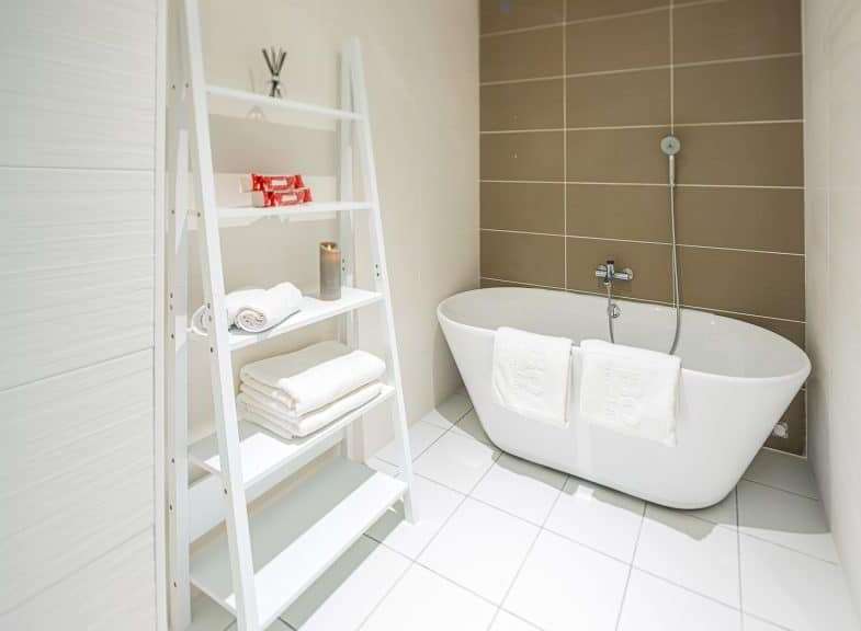 This modern bathroom features a sleek, white bathtub and stylish ladder shelving for towels and toiletries.