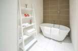 This modern bathroom features a sleek, white bathtub and stylish ladder shelving for towels and toiletries.