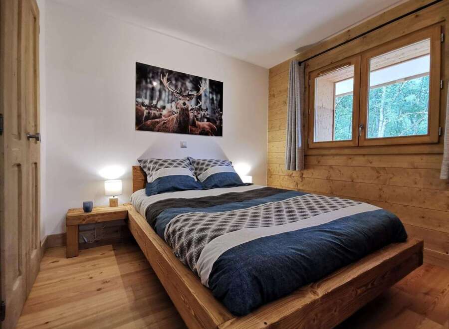 Cozy bedroom with a rustic wooden bed and a large window overlooking a forest.