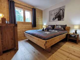 Cozy wooden bedroom with a king-size bed, featuring a rustic design and large windows offering forest views.