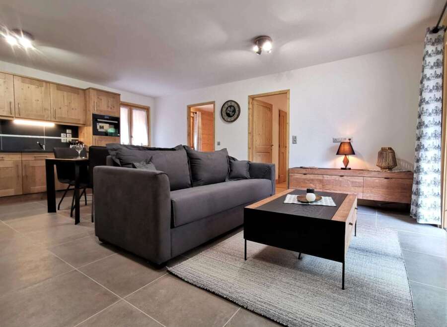 This stunning apartment boasts an open-plan living area with a comfortable grey sofa, a stylish coffee table, and a modern kitchen with wooden cabinets.