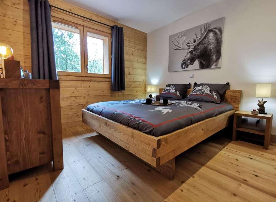 Cozy wooden bedroom with a king-size bed, featuring a rustic design and large windows offering forest views.