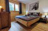Cozy wooden bedroom with a king-size bed, featuring a rustic design and large windows offering forest views.