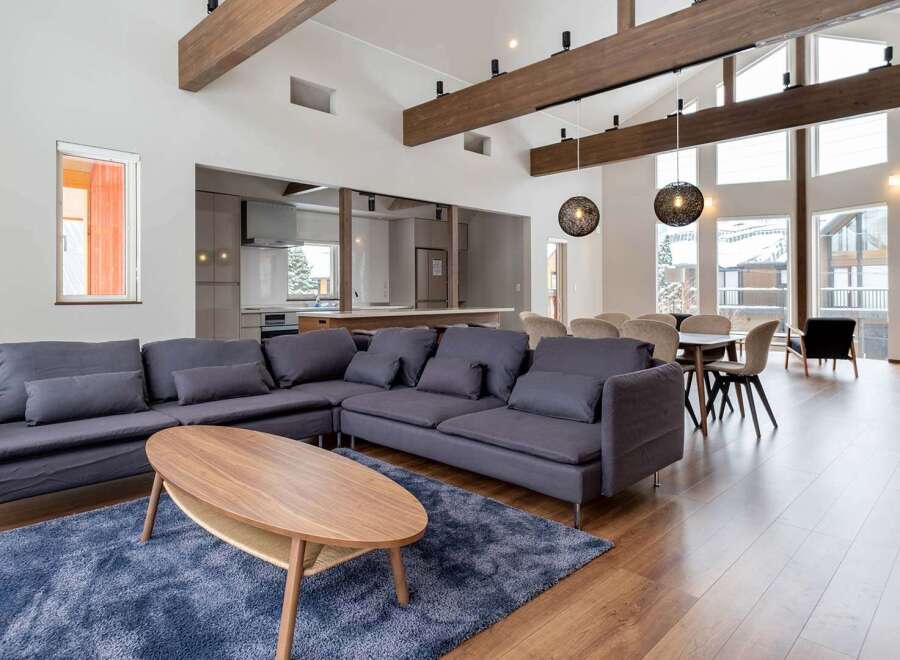 This stunning vacation home boasts an open-concept living area with floor-to-ceiling windows offering breathtaking views, hardwood floors, and a cozy sectional sofa perfect for relaxation.