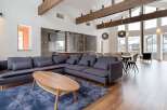 This stunning vacation home boasts an open-concept living area with floor-to-ceiling windows offering breathtaking views, hardwood floors, and a cozy sectional sofa perfect for relaxation.