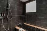 Modern bathroom with dark tile, built-in wooden bench, and rainfall shower head.