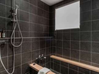 Modern bathroom with dark tile, built-in wooden bench, and rainfall shower head.