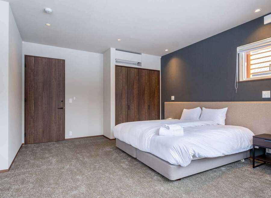 This modern bedroom boasts a king-size bed with crisp white linens, a plush beige headboard, and a convenient bedside table.