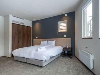 This modern bedroom boasts a comfortable king-size bed with plush bedding, a spacious closet, and large windows offering ample natural light.
